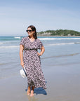 Woman in a floral dress standing on a beach with ocean waves and sky in the background