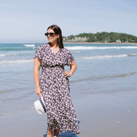 Woman in a floral dress standing on a beach with ocean waves and sky in the background